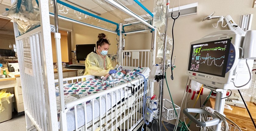 A photo shows a nurse with a stethoscope checking on an infant inside a hospital intensive care unit.