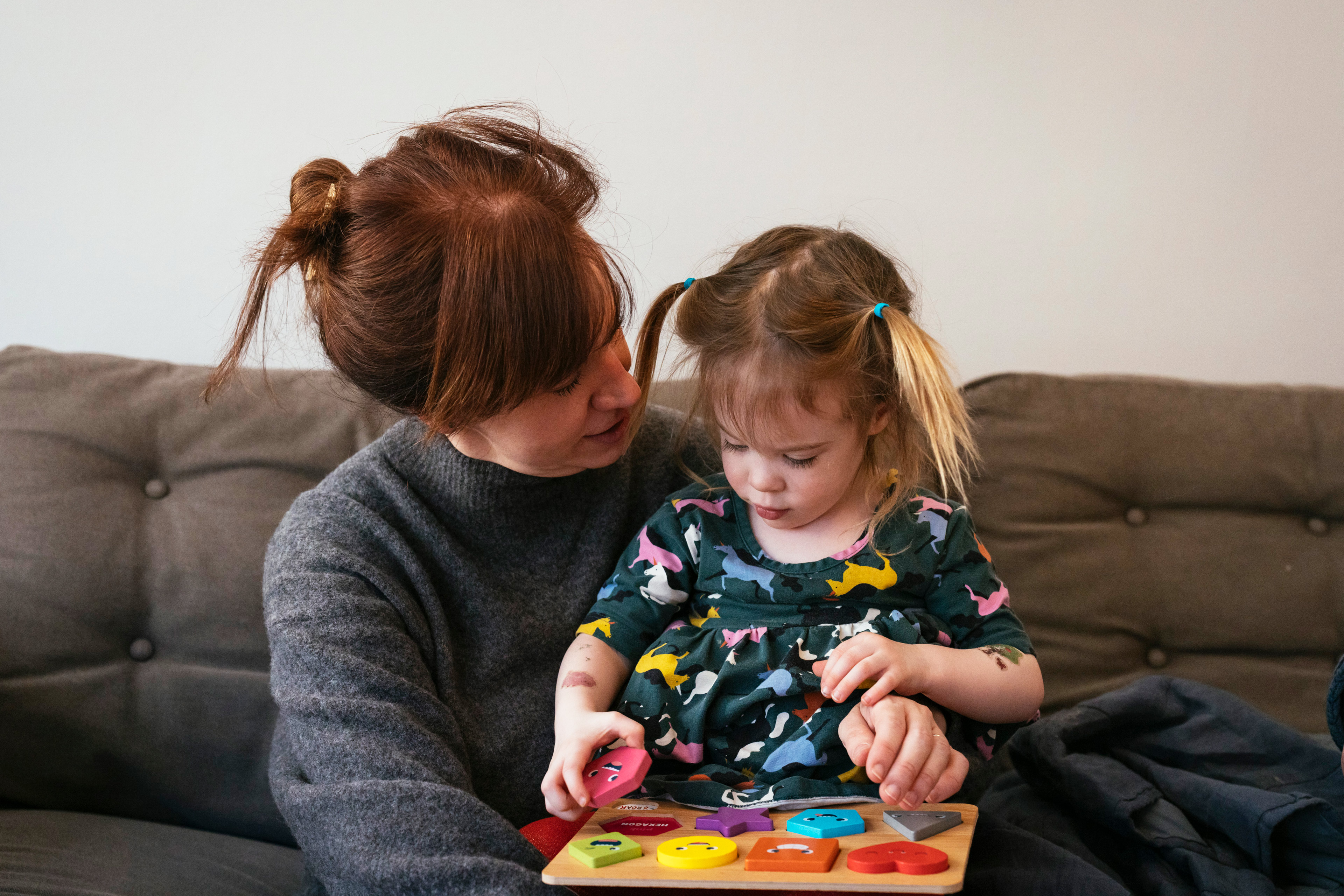 A photo shows Brenna Kearney and daughter Joey sitting on a couch together. Joey is playing with colorful block toys.