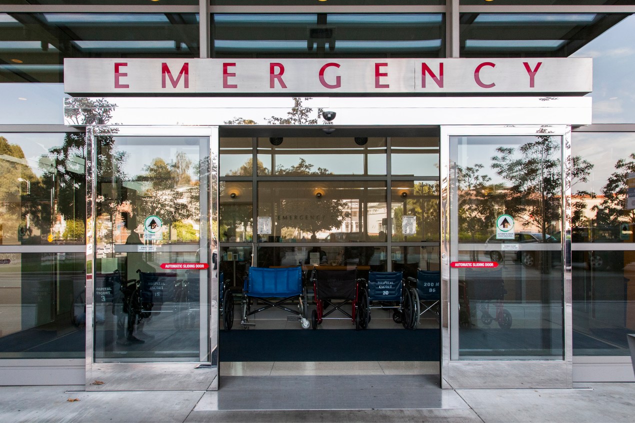 A daytime photograph of the outside of the outside sliding doors of an emergency room.
