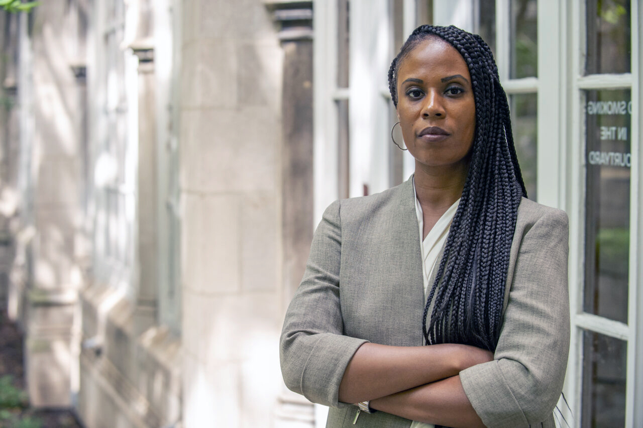 Jamelia Morgan, a professor at Northwestern University Pritzker School of Law, stands in a grey suit and looks directly at the camera with her arms folded comfortably across her chest.