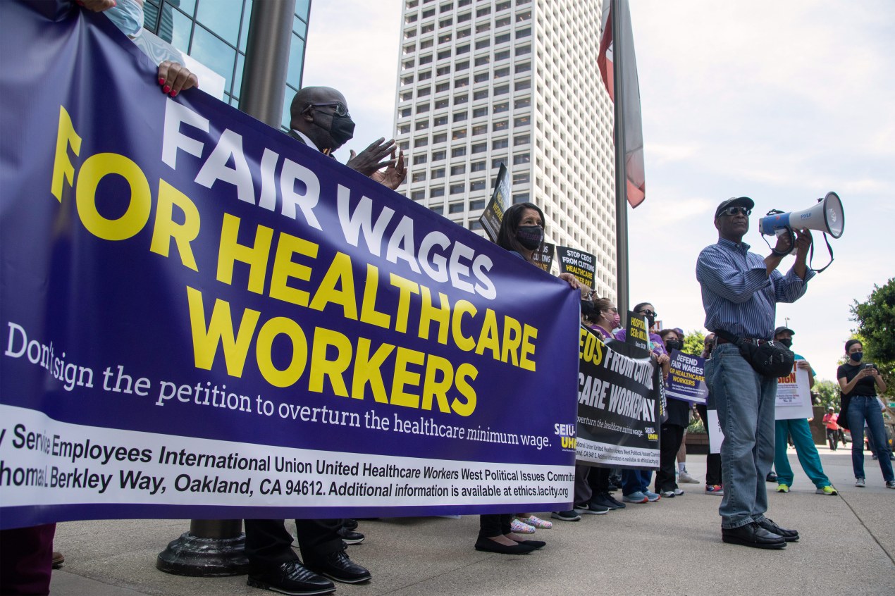 A photo shows protesters gathered outside a building. A group hold a banner that reads, "Fair wages for healthcare workers."