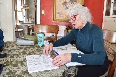 A photo shows a woman sitting at a table and flipping through a binder of paperwork.