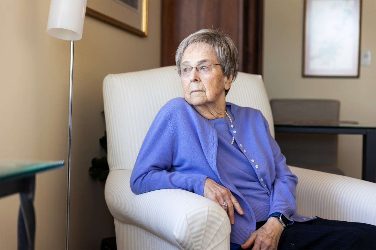 A photo shows an older woman sitting in a chair and looking to the left.