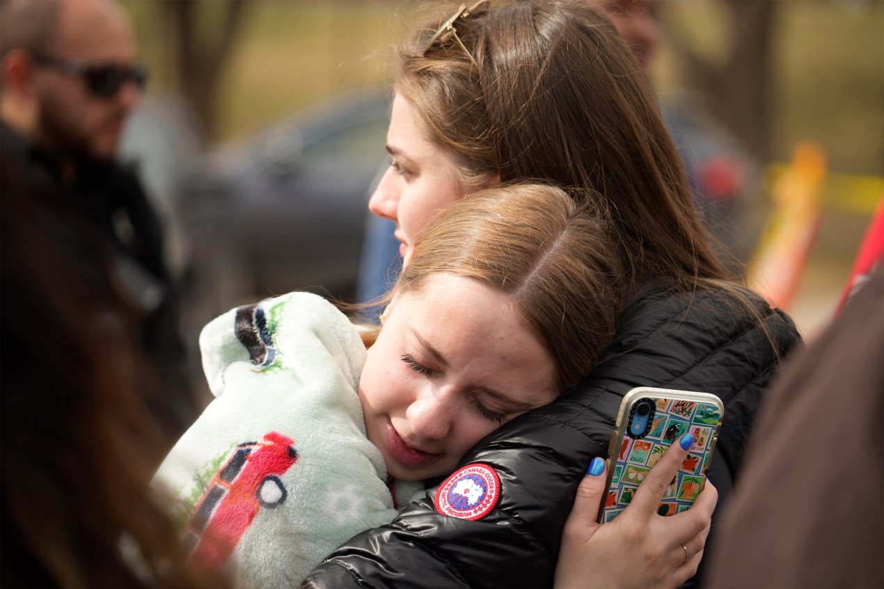 A photo of two women hugging outside of East High School in Denver after a shooting.
