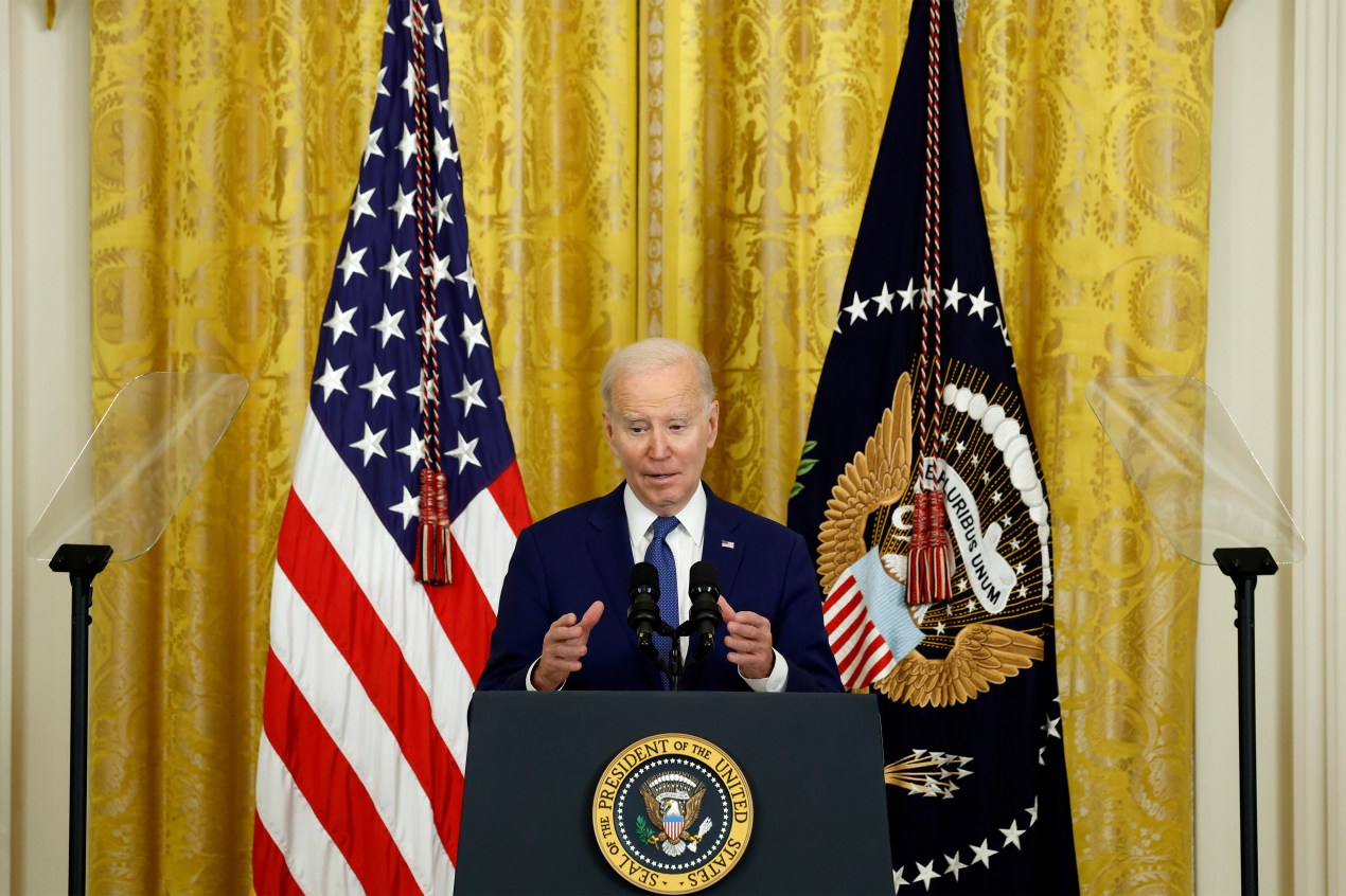 A photo of Biden speaking at a podium inside the White House.