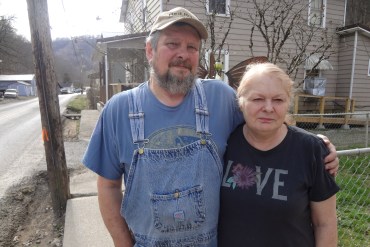Michael and Liz Williams stand on a sidewalk outside. Michael has his arm wrapped around his wife, Liz.