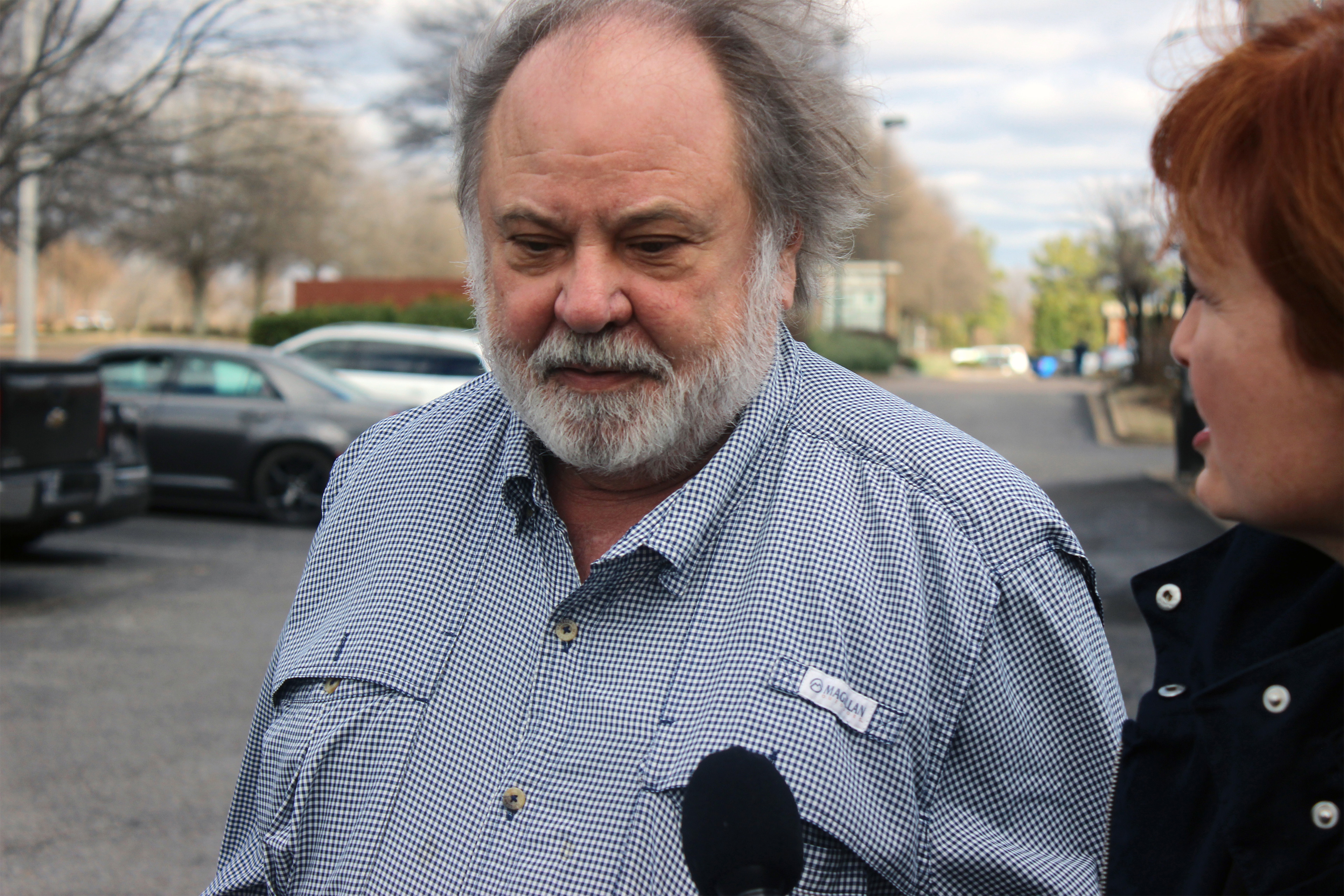 A photo shows a man walking outside as a reporter holds a microphone in front of him.