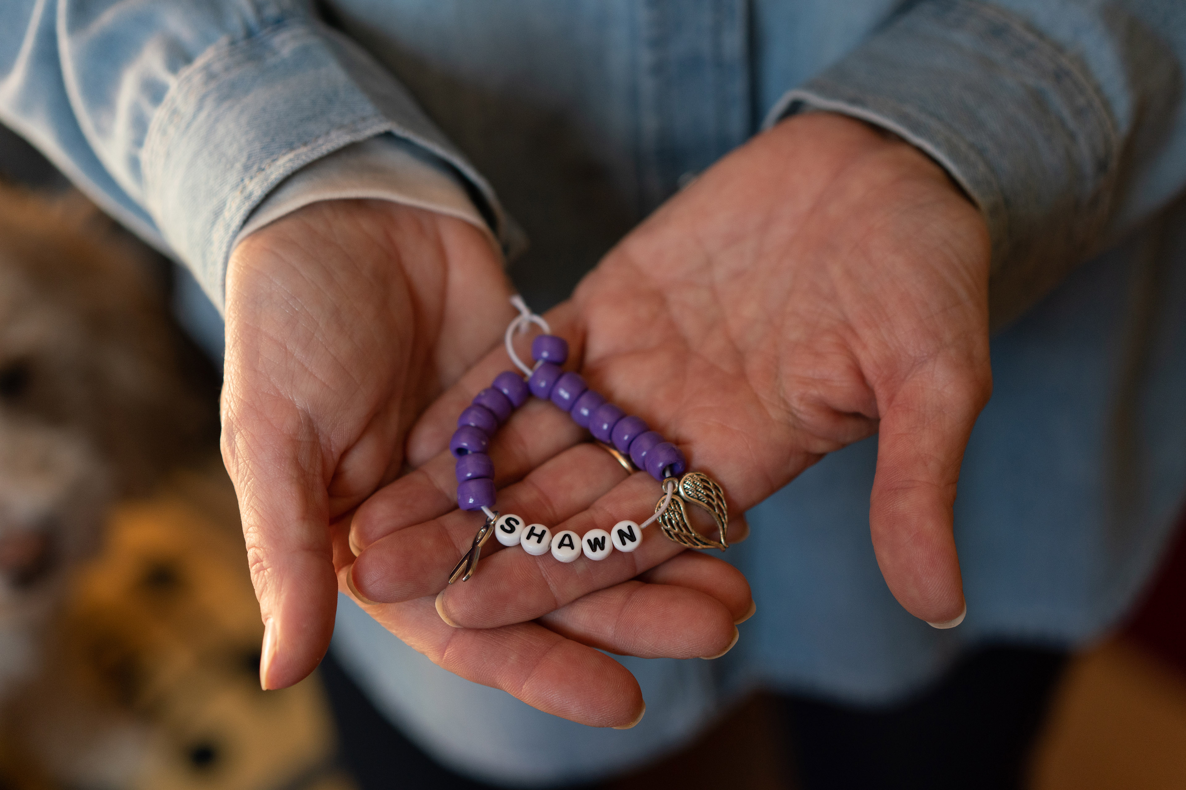 A close-up image of two hands holding a purple beaded bracelet with letter beads spelling "Shawn".