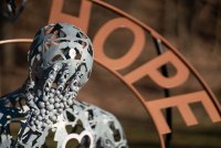 A close-up image of a metal statue of a person leaning their head on their hand. Slightly out of focus behind the figure is the word "Hope" in copper -- another part of the statue.