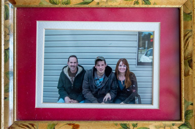 In a yellow frame painted with flowers is a photo of a young man sitting between two older adults outside the wall of a building.