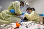 A dentist and dental assistant perform dental work on a patient.