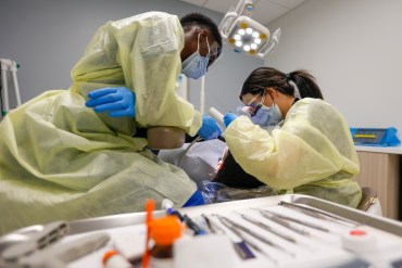 A dentist and dental assistant perform dental work on a patient.