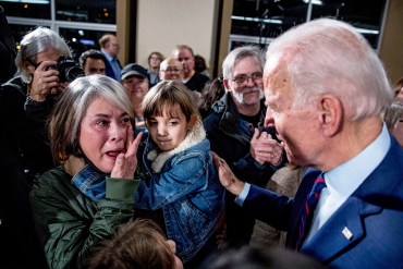 A photo shows a woman wiping away tears while speaking to Joe Biden at an event. She is holding a young girl in her arms.