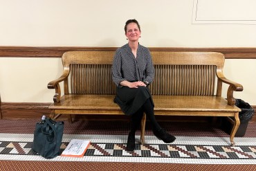 A photo of a woman sitting for a portrait on a bench indoors.