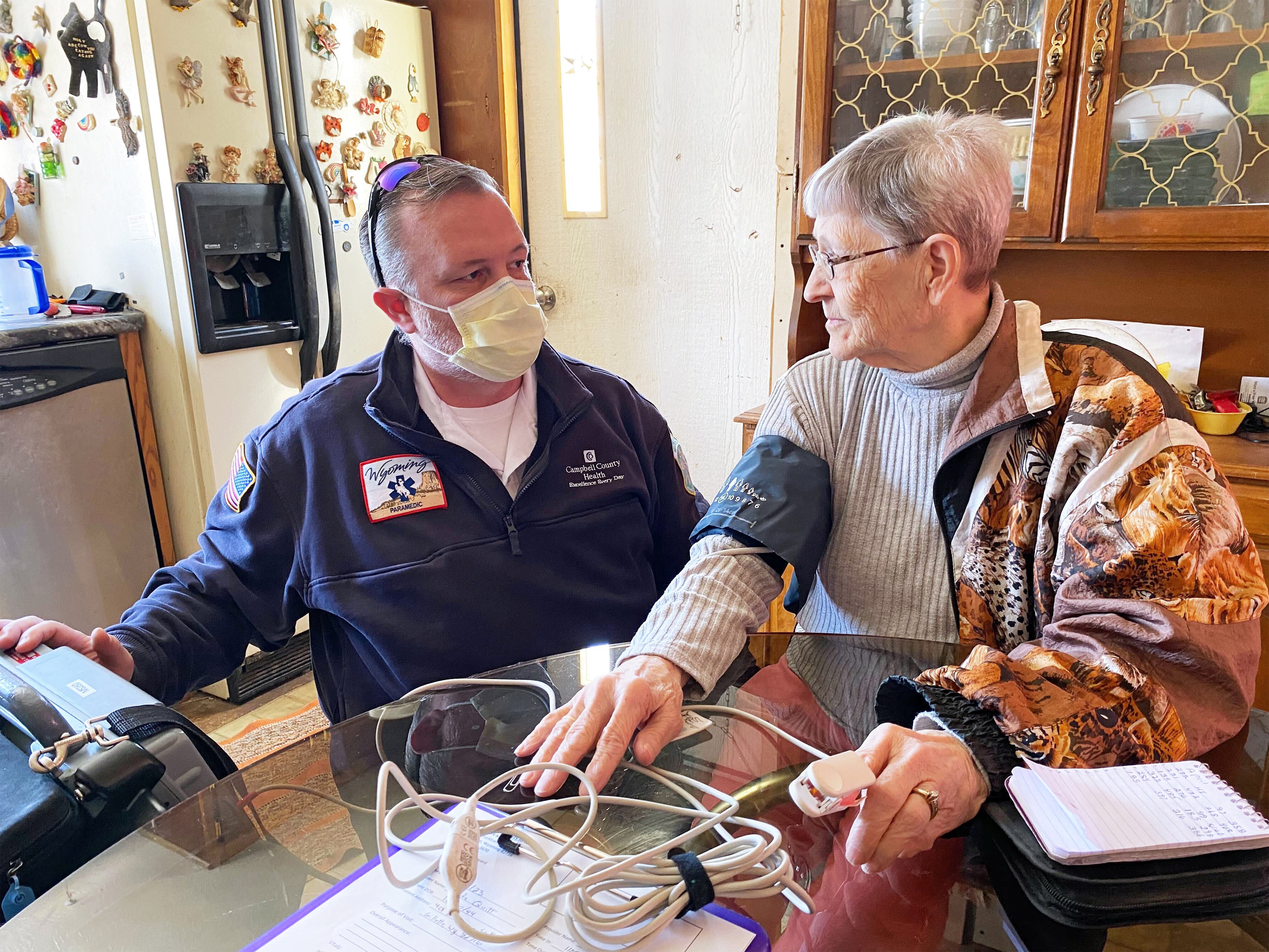 A photo of a paramedic checking a woman's pulse in her home.