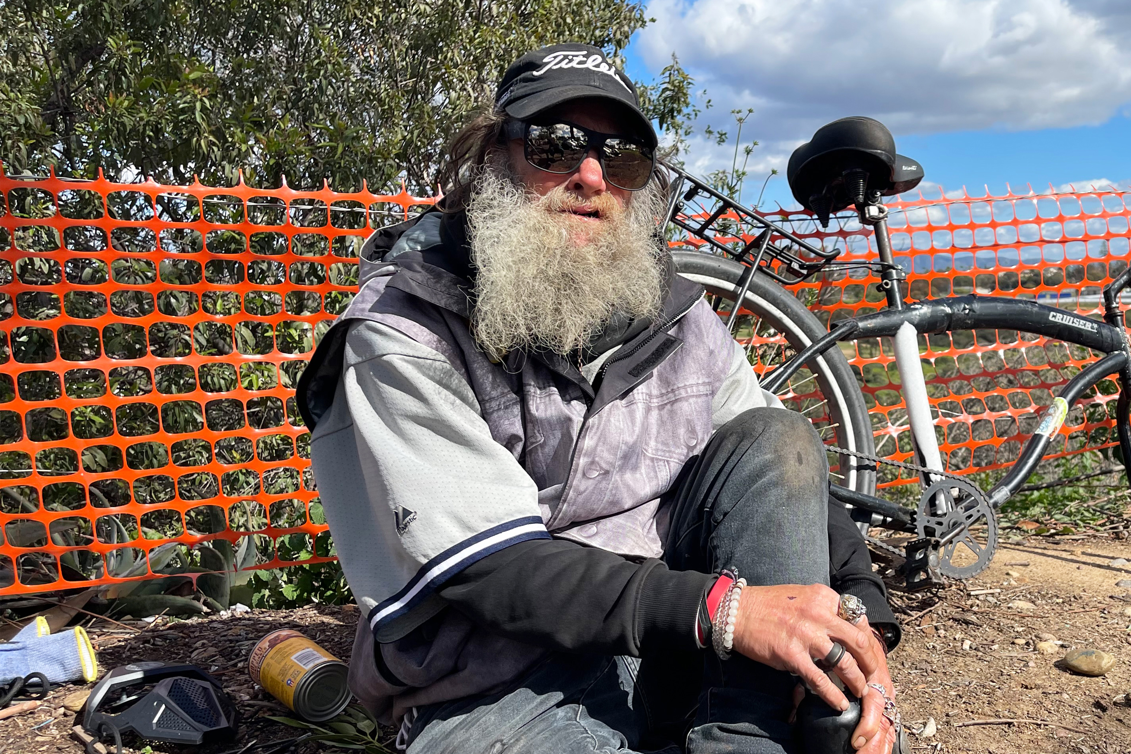 A photo of a man sitting on the side of a road next to a bicycle.