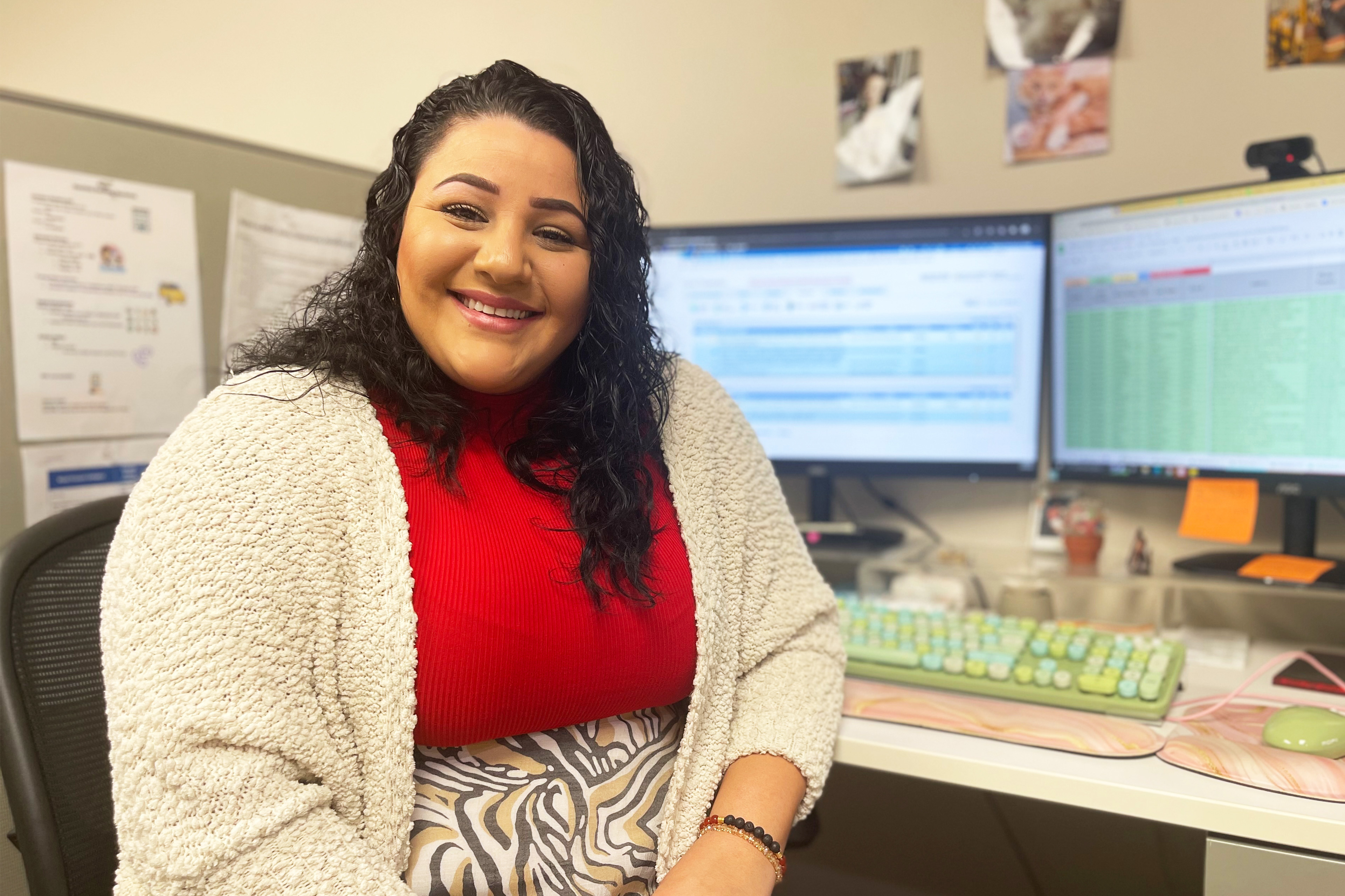 A photo of a woman posing for a portrait at a desk with a computer.