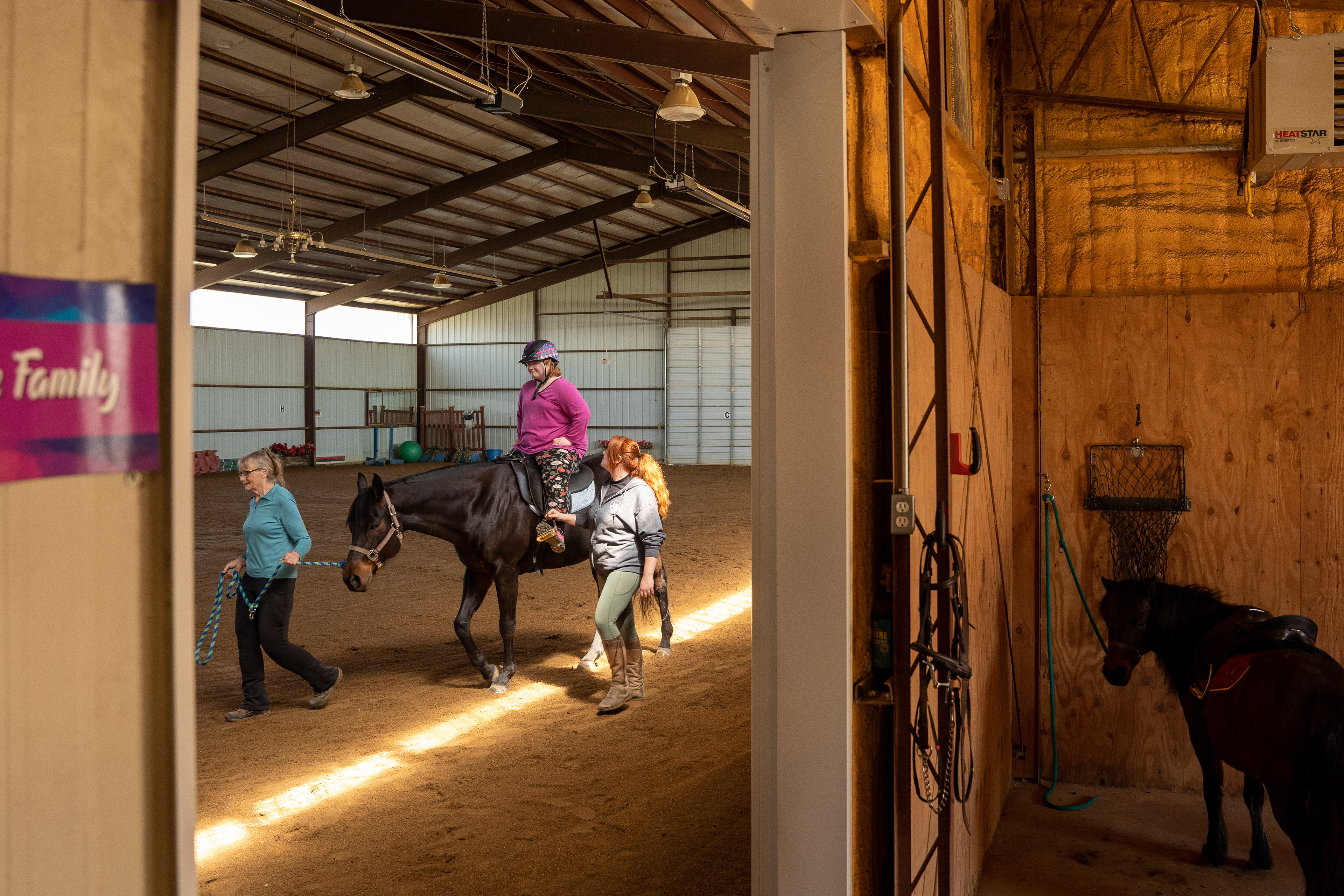 A photo of a young woman on a horse being led around a barn.