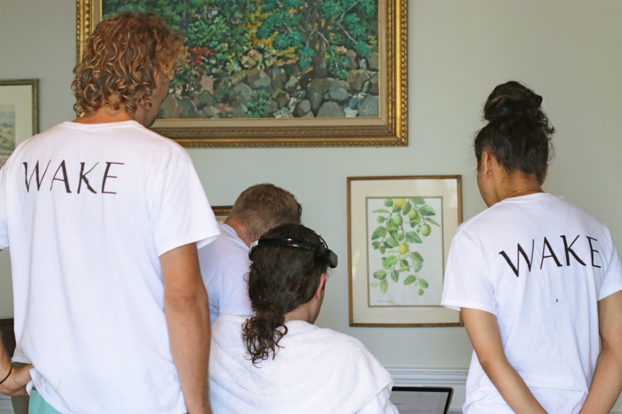 A photo of two employees wearing white t-shirts with Wake Network's logo overseeing a man looking at a computer screen with a device on his head.