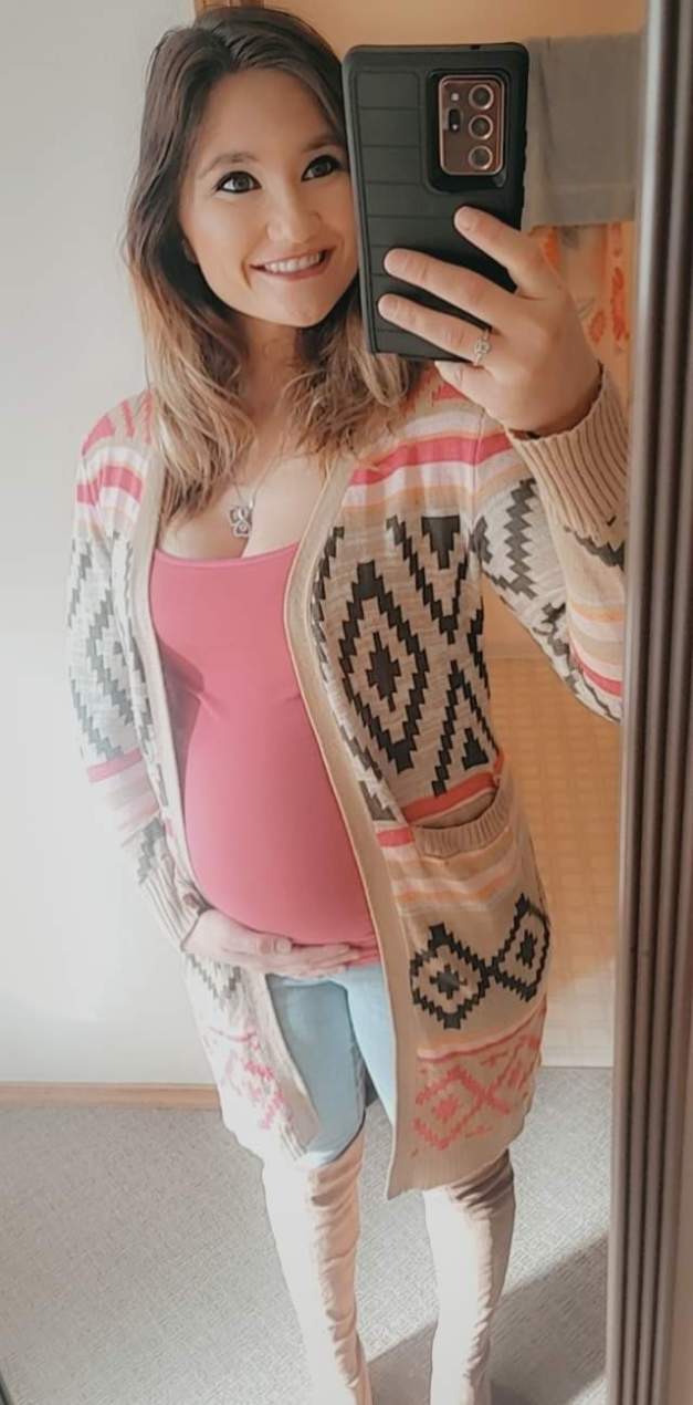 A selfie-style photo of Kaitlyn Anderson. She smiles up at her camera while holding her belly, so the viewer can immediately tell she is pregnant.