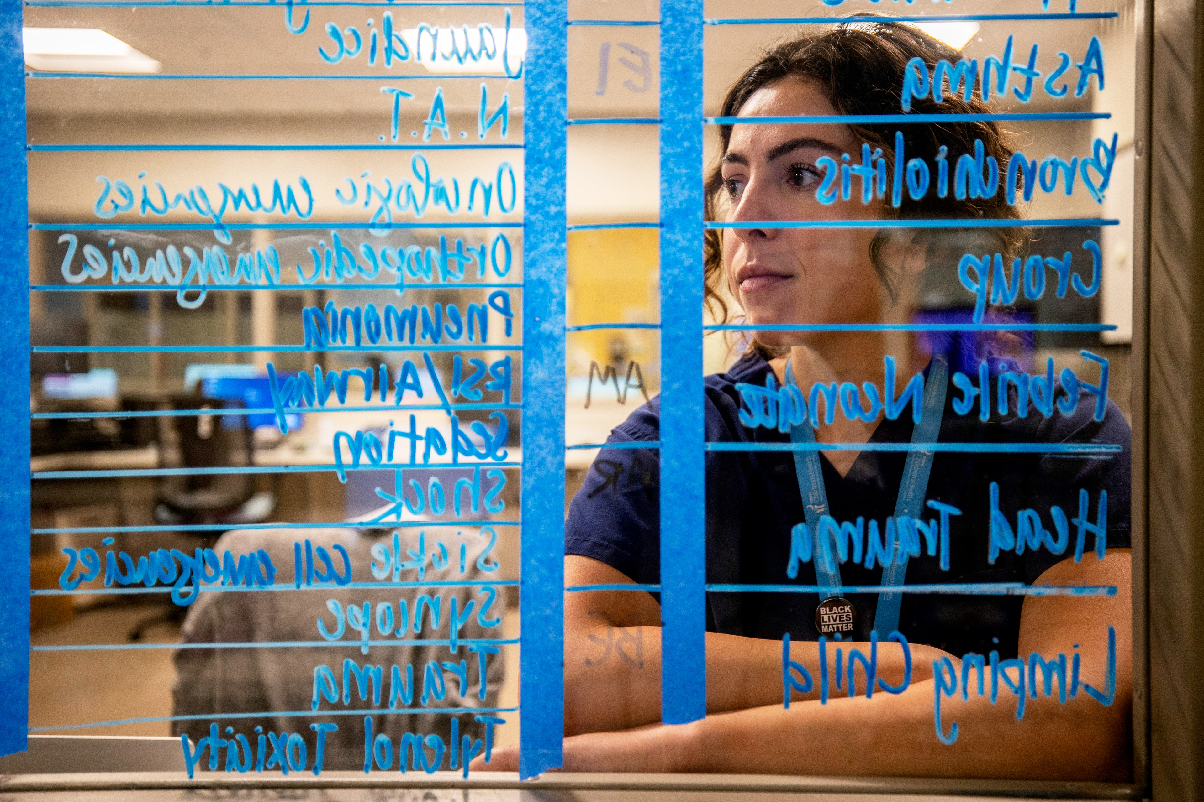 A photo of Melanie Gray Miller posing for a portrait behind a clear dry-erase board. Blue writing obscures some of her face.