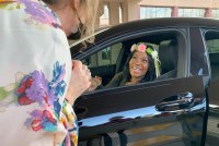 A photo of a woman wearing a floral tiara smiling inside her car.