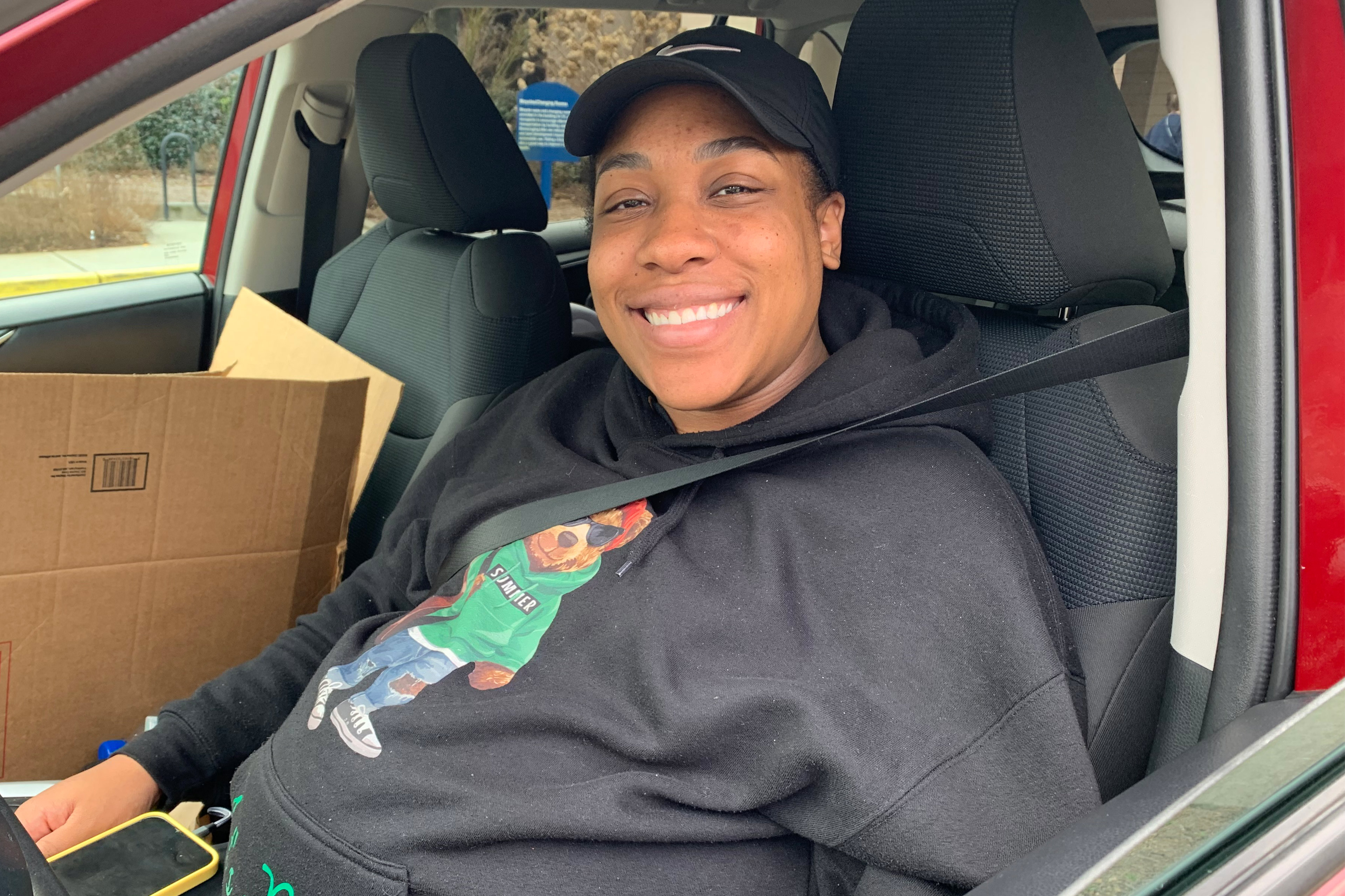 A photo of a pregnant woman smiling for a photo while sitting in her car.