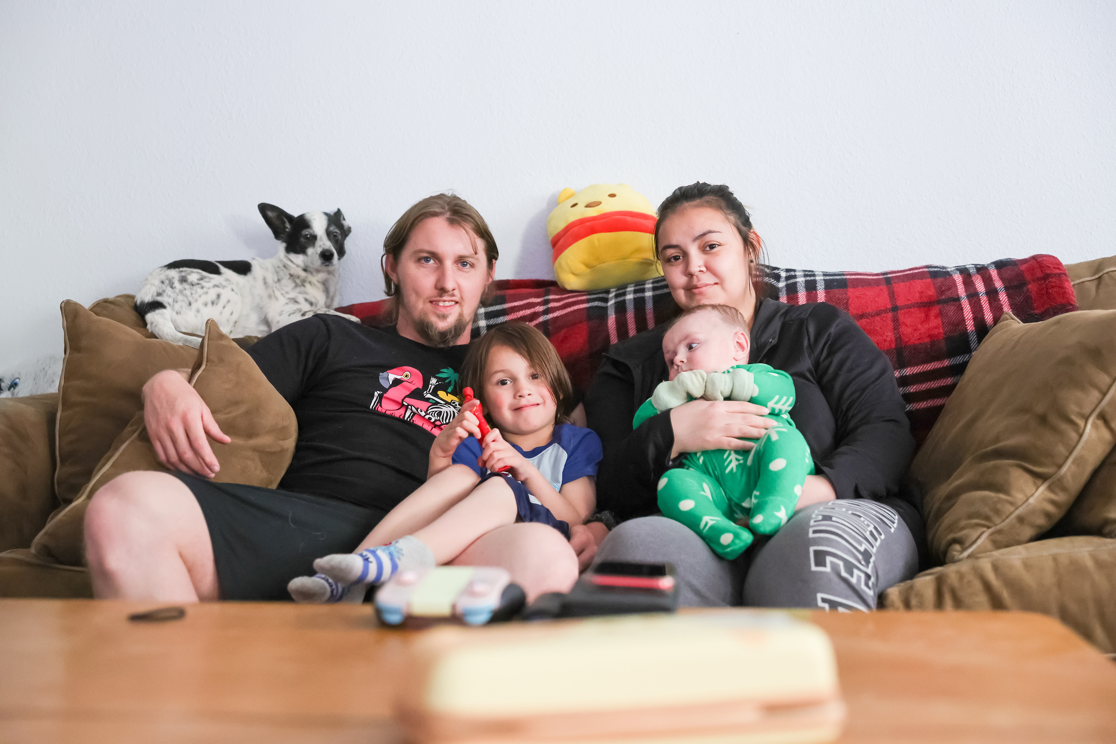 Jade Vandiver sits with her husband, Zane, and sons, Zachary (left) and Ezra (right), and their small dog. They are on a couch in their home.
