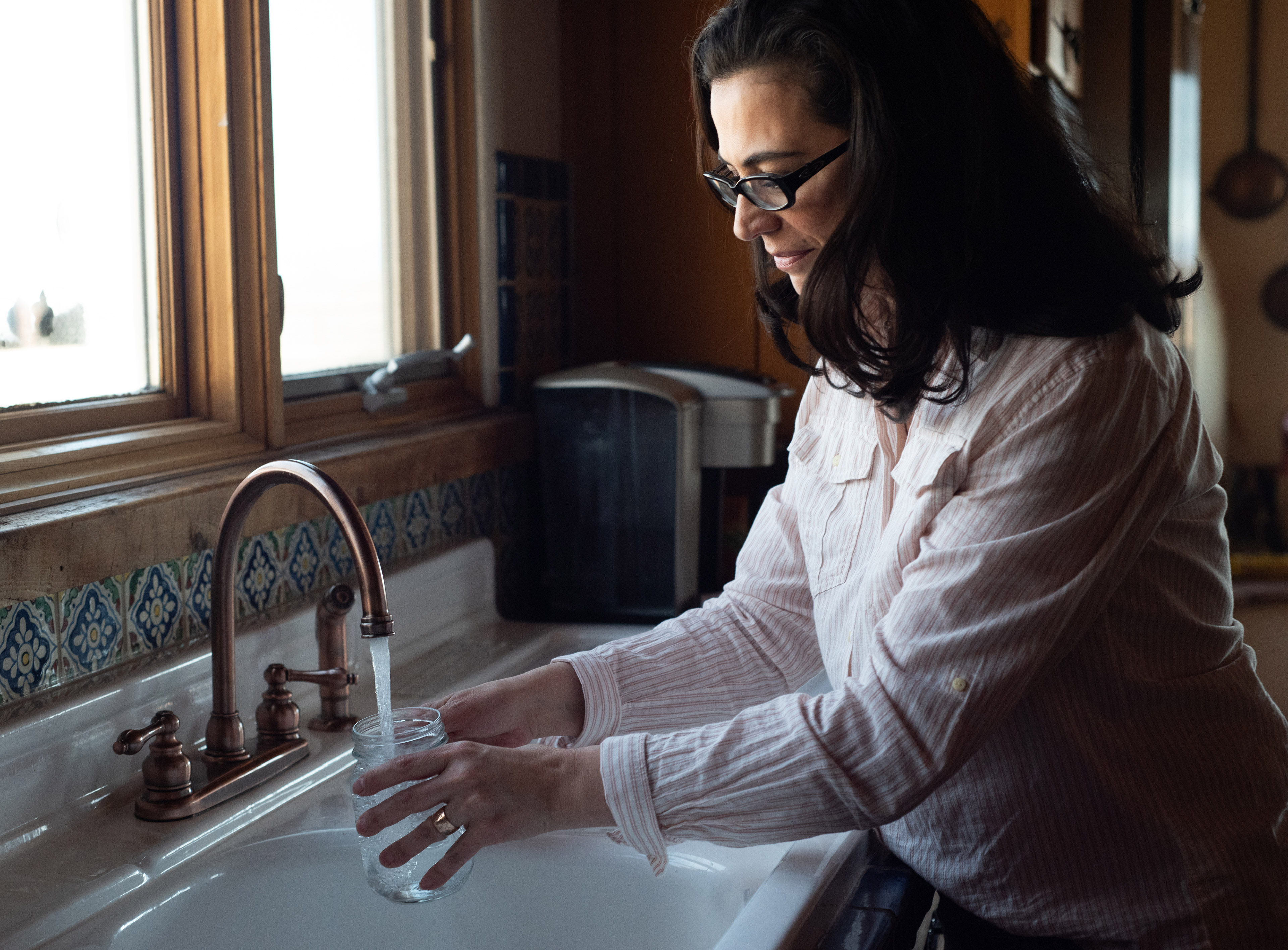 A photo of Julie Zahringer filling a mason jar with water from her kitchen sink.