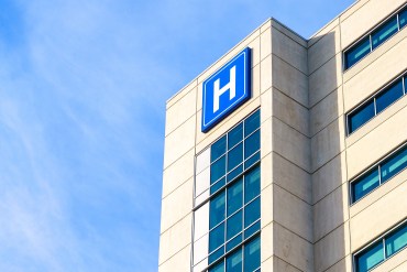 A photo of the exterior of a hospital building marked with a large, blue and white H.