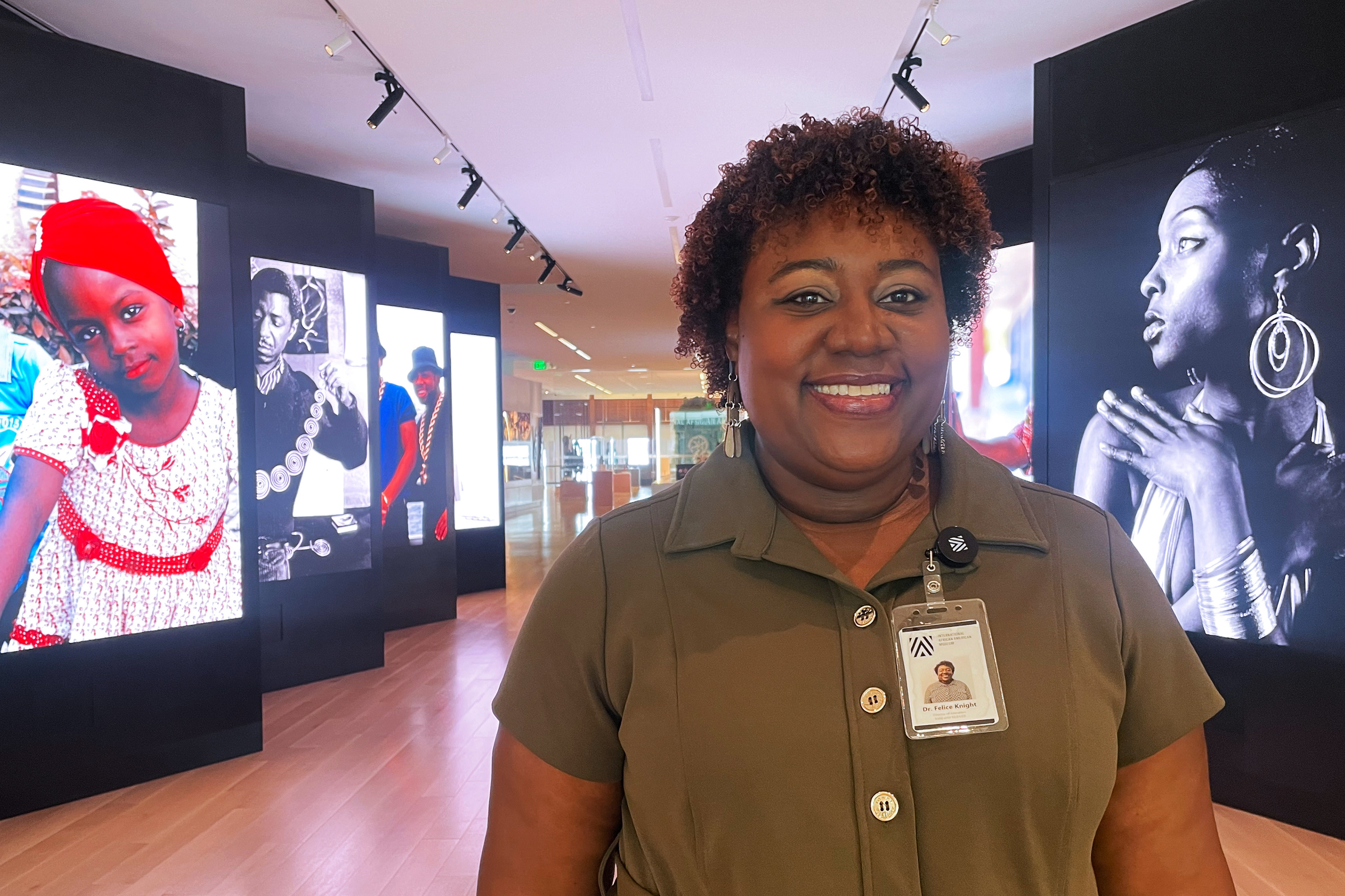 A photo of a woman standing inside a museum. Photos from history are displayed on screens behind her.