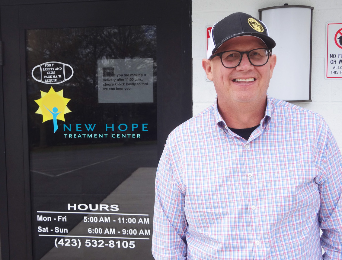 A photo of a man standing outside by a door with text on that reads, "New Hope Treatment Center."