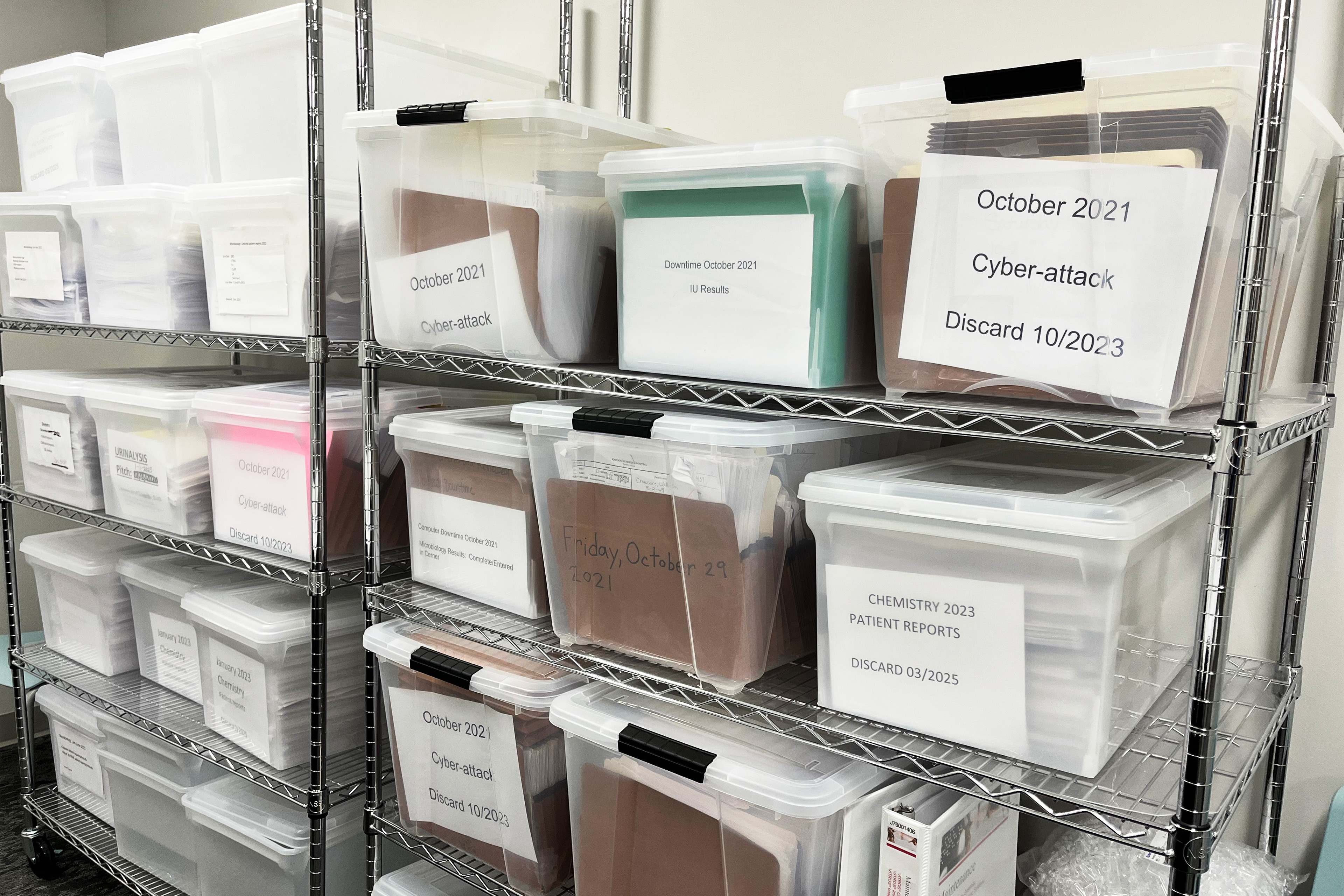 A photo of clear plastic bins filled with paper medical records in file folders.