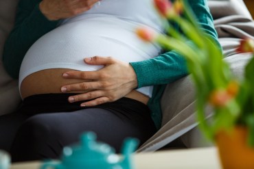 A close up photograph of a pregnant woman's belly. There are orange tulips blurred in the foreground.