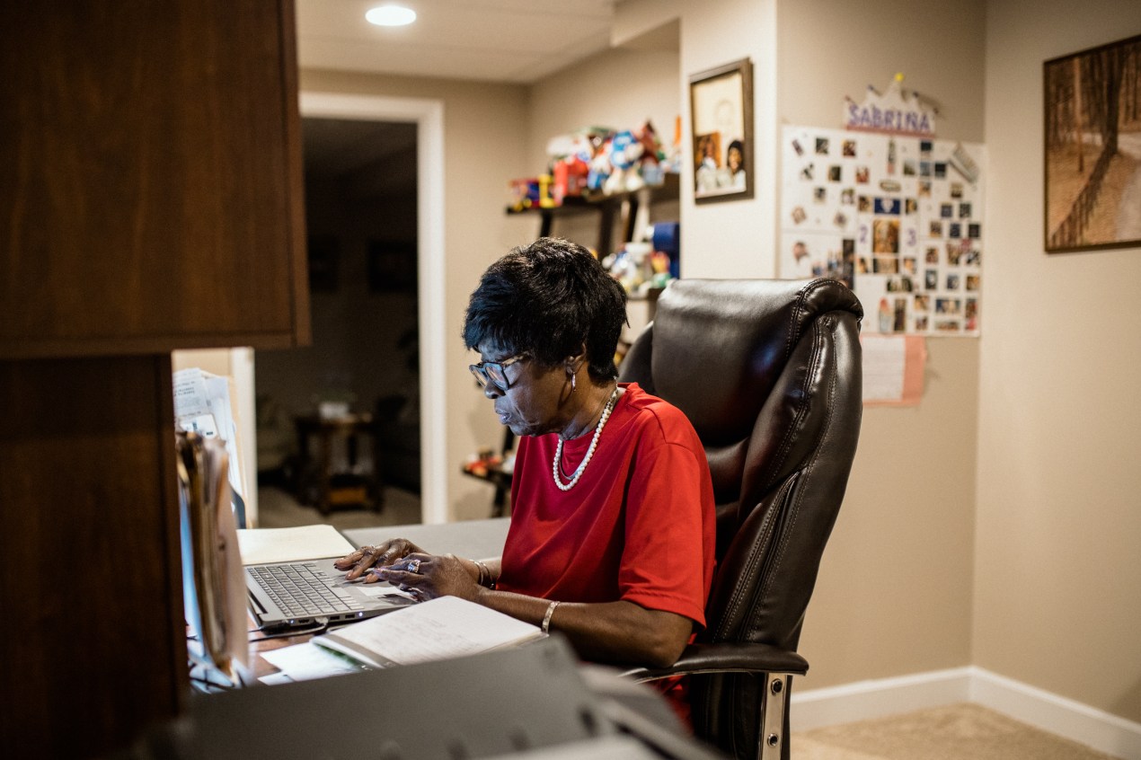 Bluizer Greene is sitting at her a desk in her home office as she works on a laptop The glow from the active computer screen softly lights the profile of her face