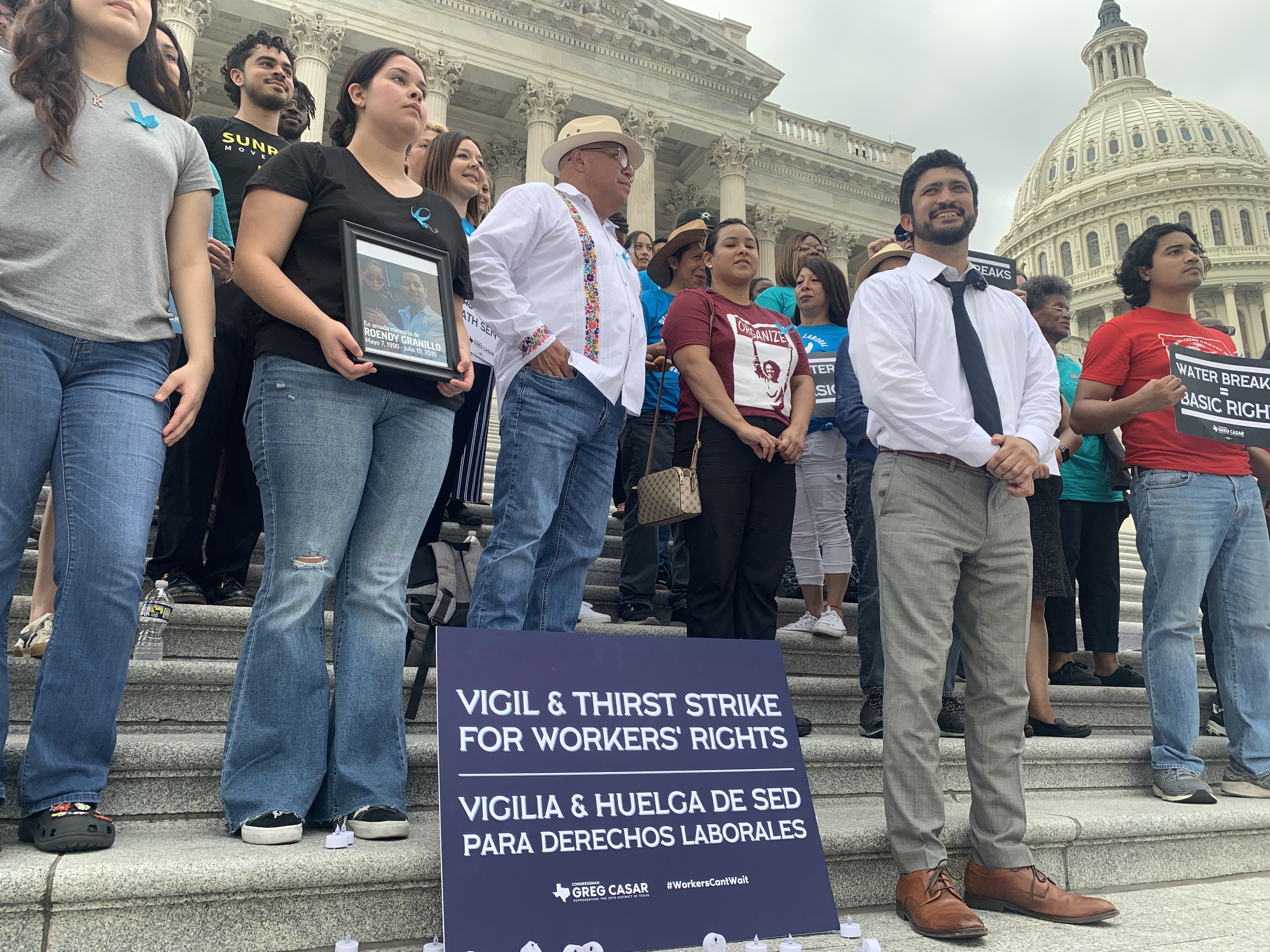 Rep. Greg Casar stands amongst a crowd of protesters at the U.S. Capitol. A sign in front of the group reads, "Vigil & thirst strike for workers' rights | Vigilia & huelga de sed para derechos laborales"