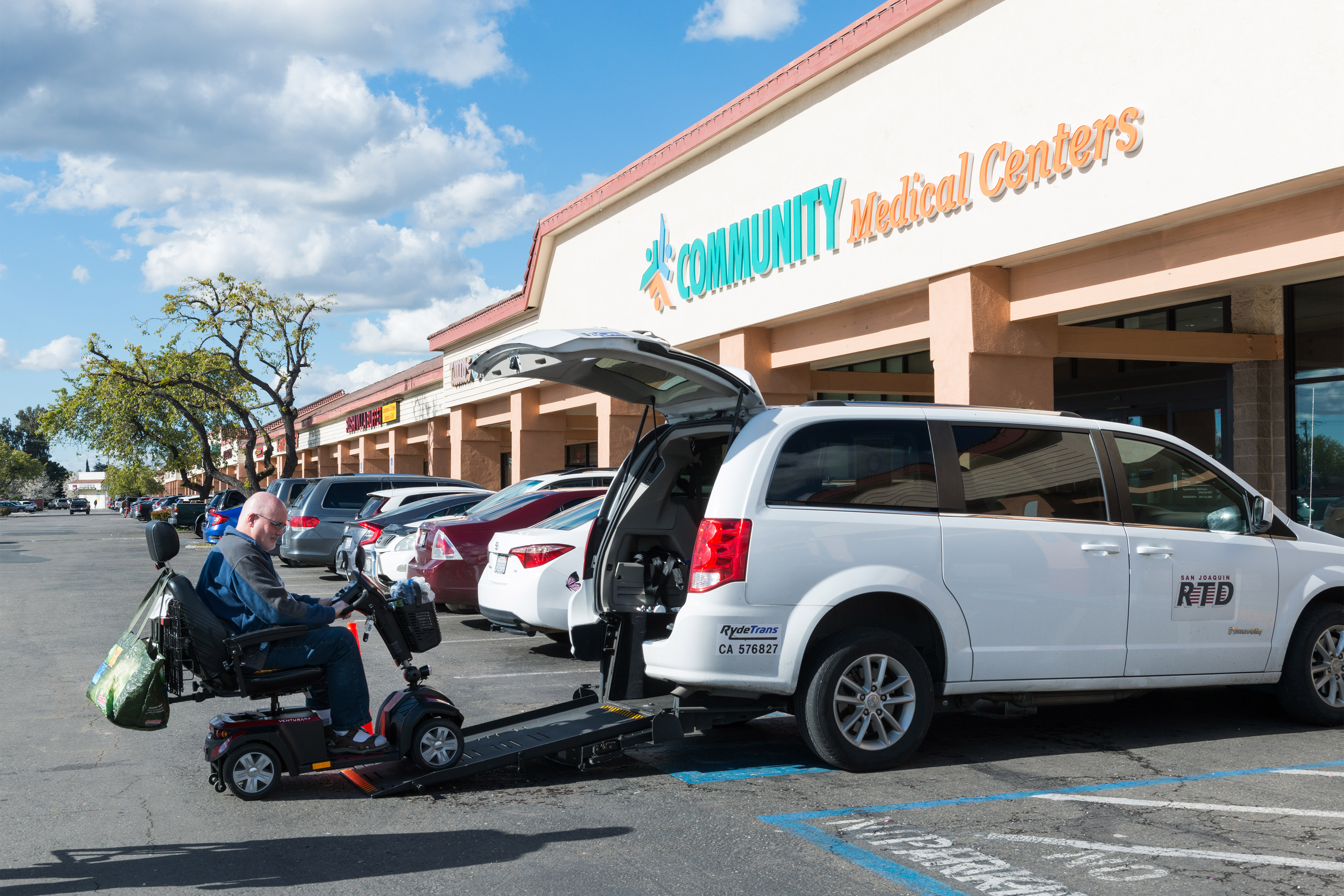 A photo of a man in a scooter backing out of a van in a parking lot.