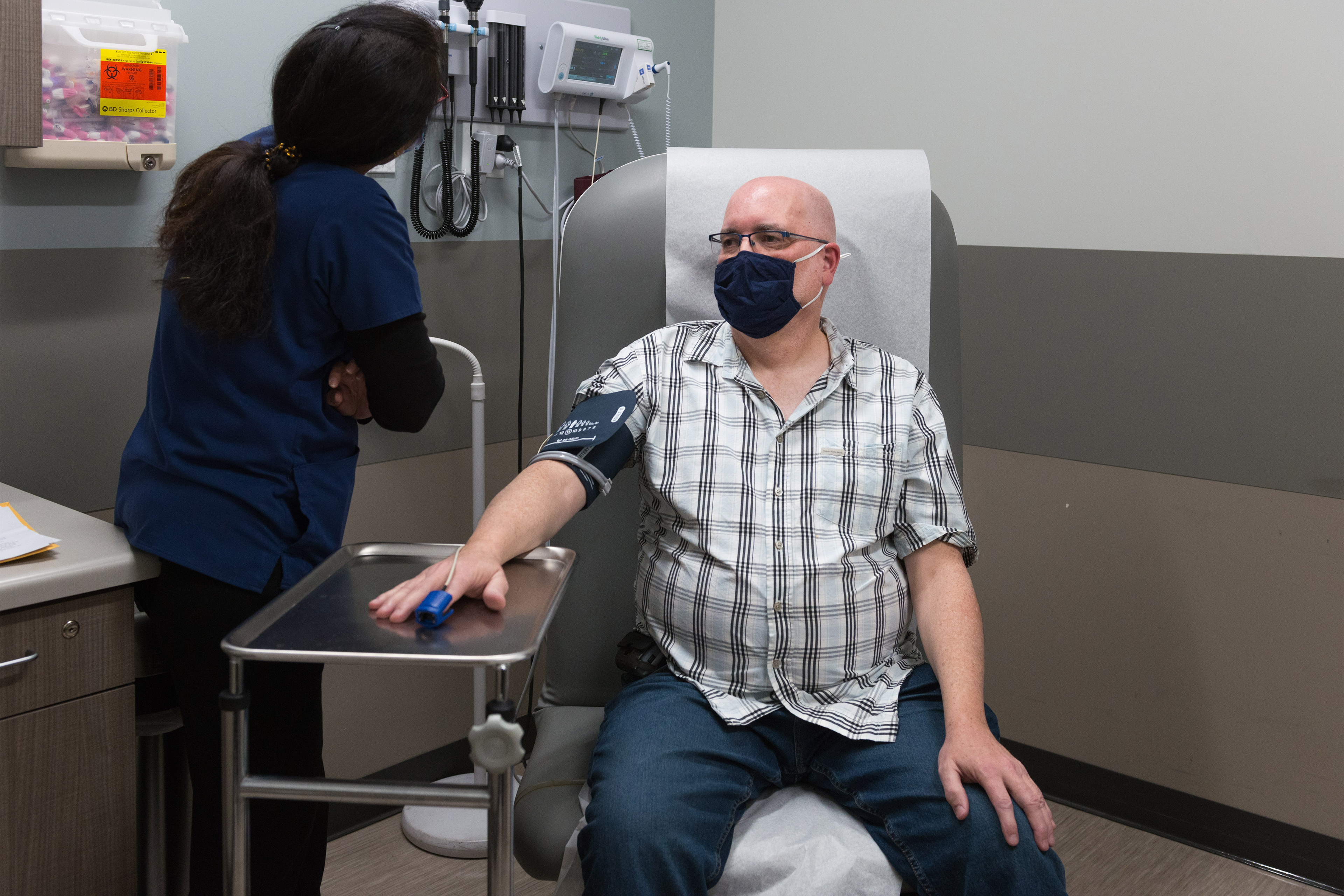 A photo of a man sitting in a chair with a blood pressure cuff around his arm and a pulse oximeter on his finger.