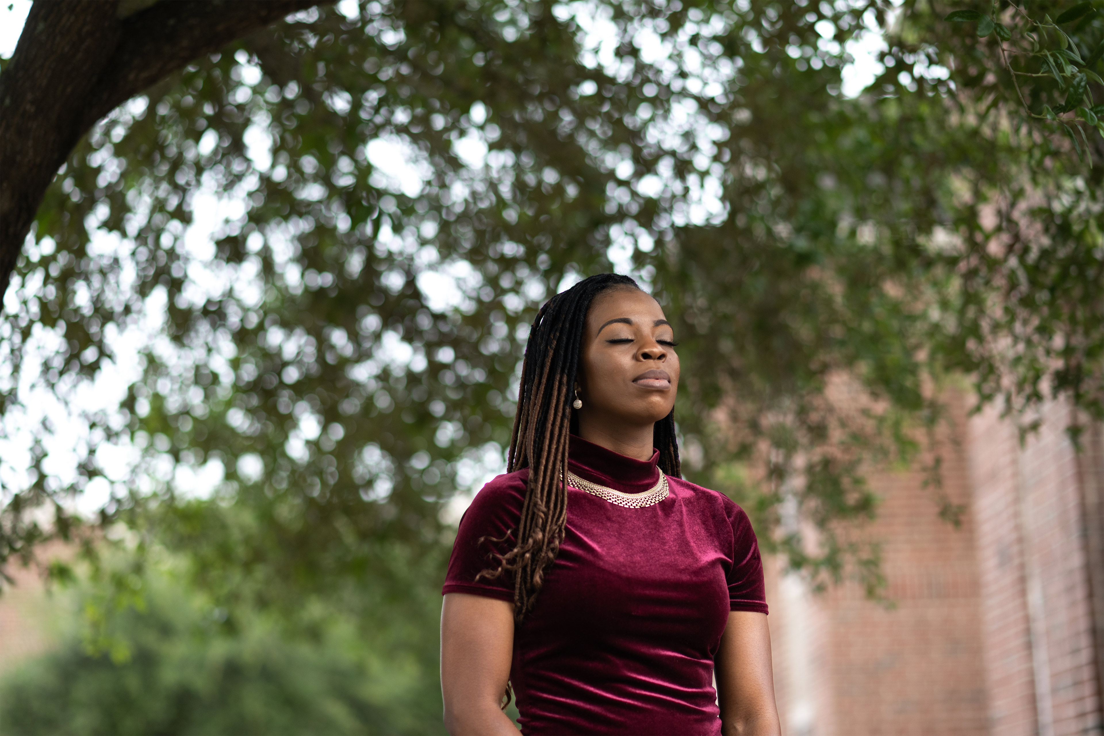 A portrait of a Black woman standing outside with her eyes closed.