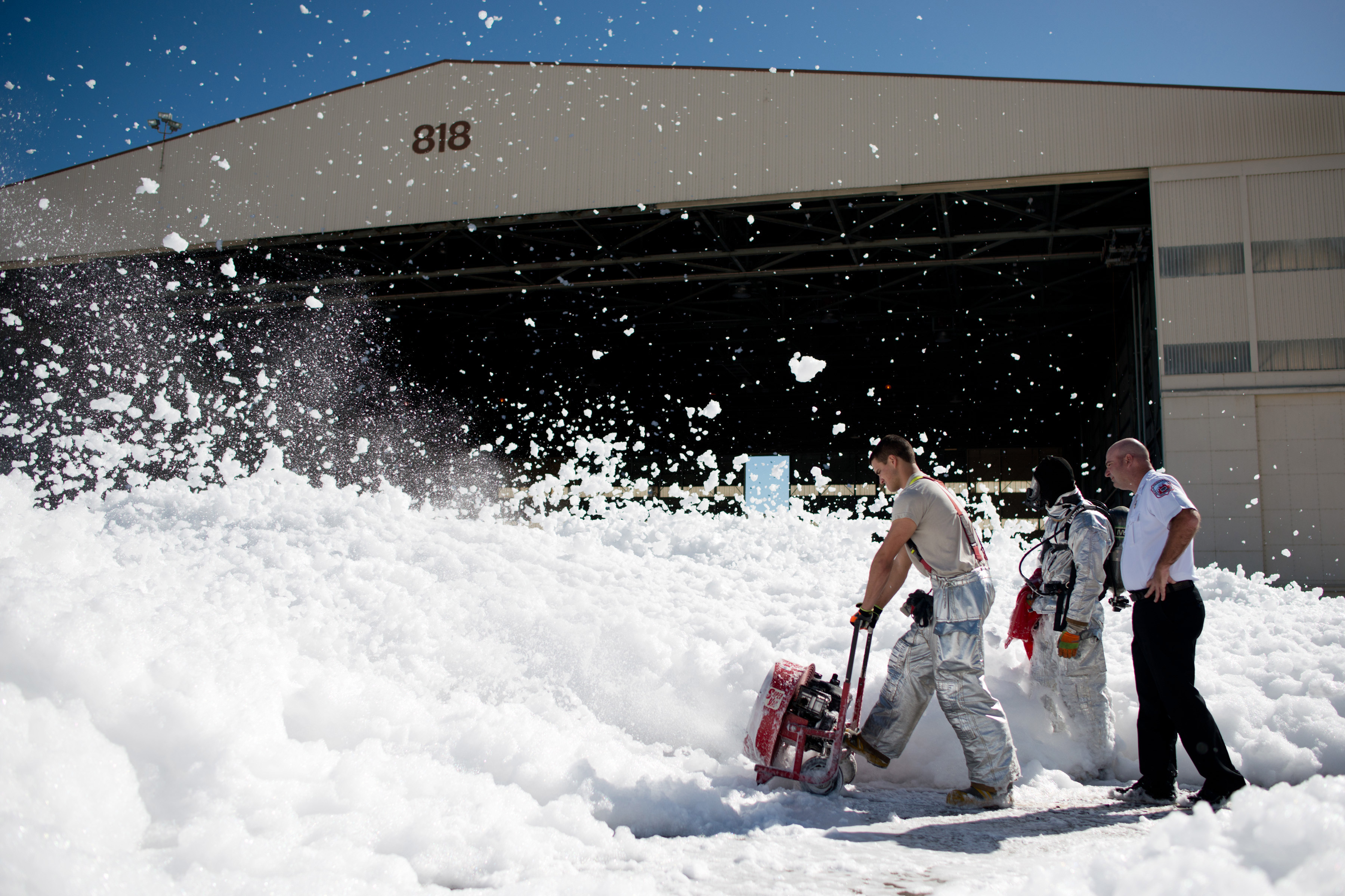 A photo of military firefighters using fans to blow away fire retardant foam.