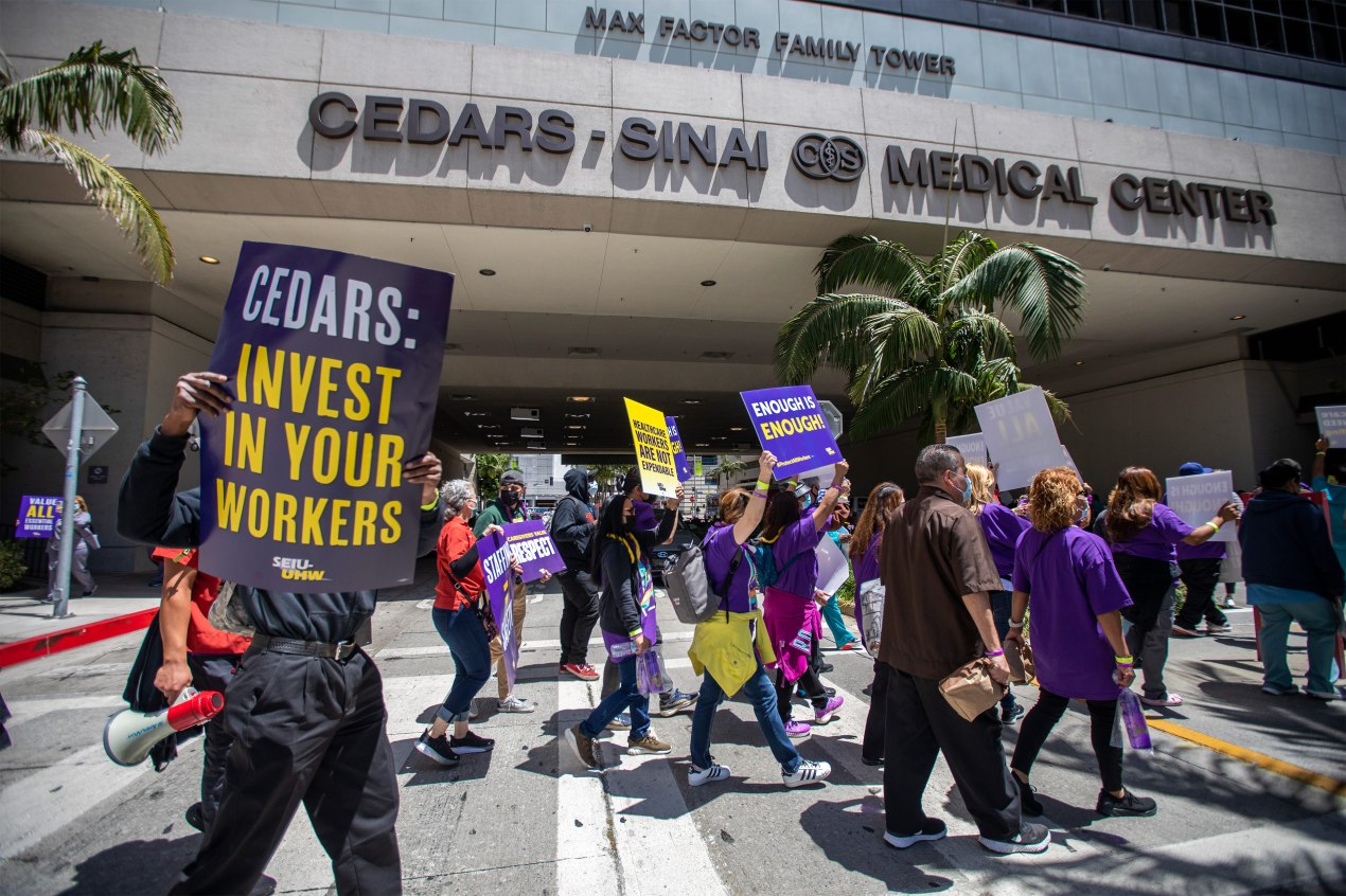 A photo of protesters holding signs that read, "Cedars: Invest in your workers," in front of a hospital.