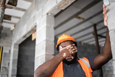 A photo of a construction worker covering his face with his hand while working outside.