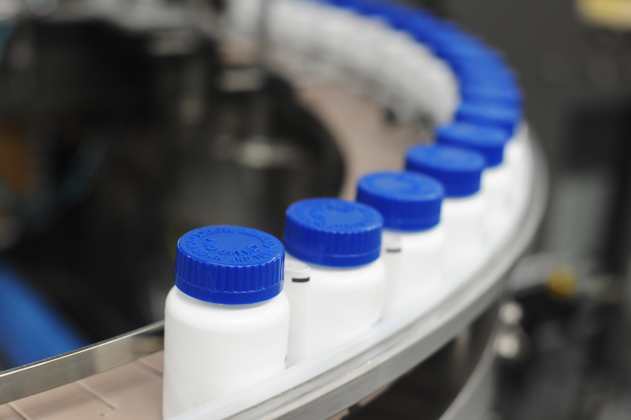 A photo of drug bottles moving on a curved conveyor belt in a factory.