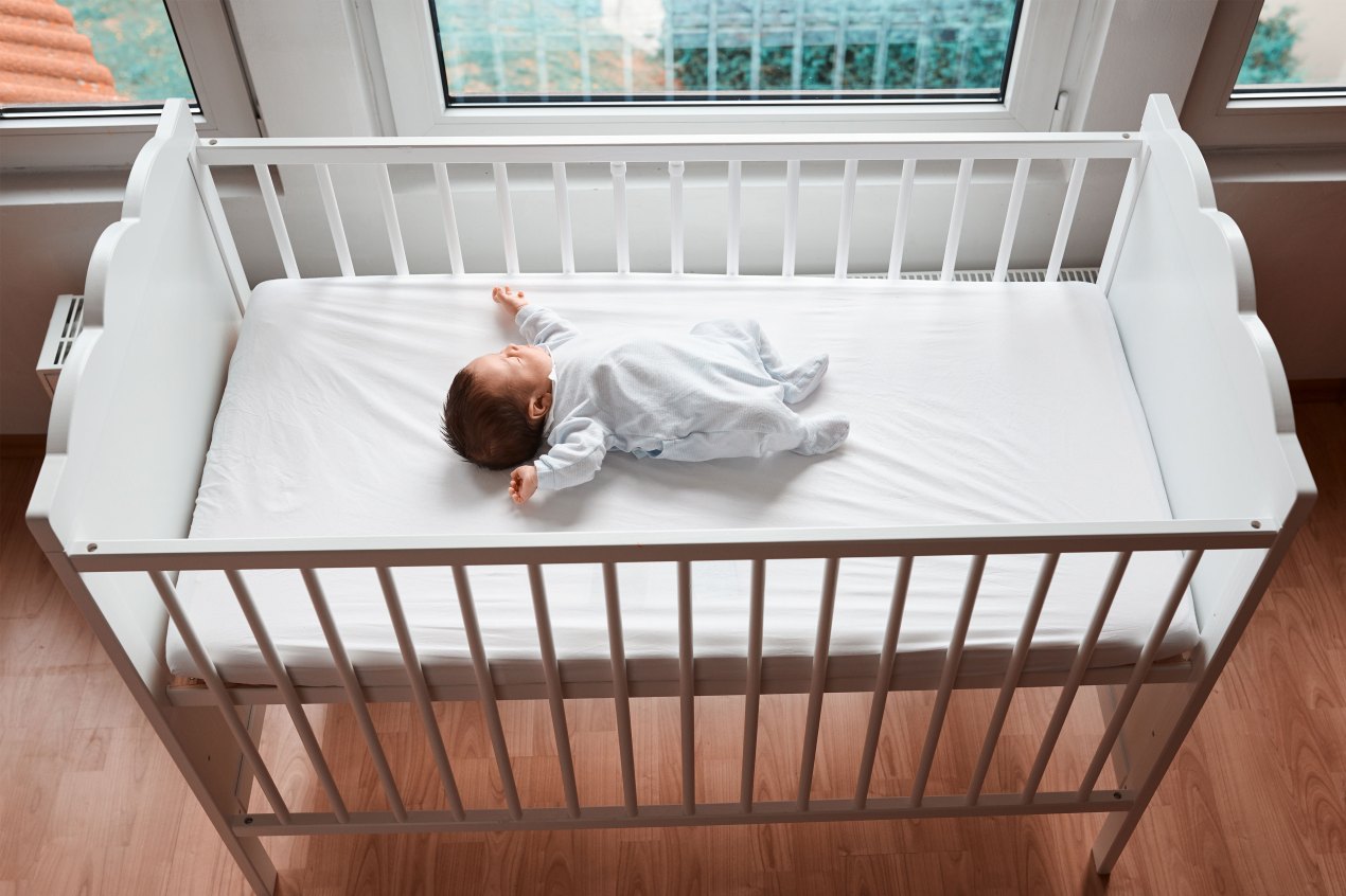 A photo of an infant sleeping in a crib on their back without blankets or pillows.
