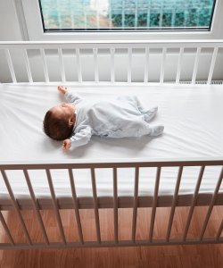 A photo of an infant sleeping in a crib on their back without blankets or pillows.
