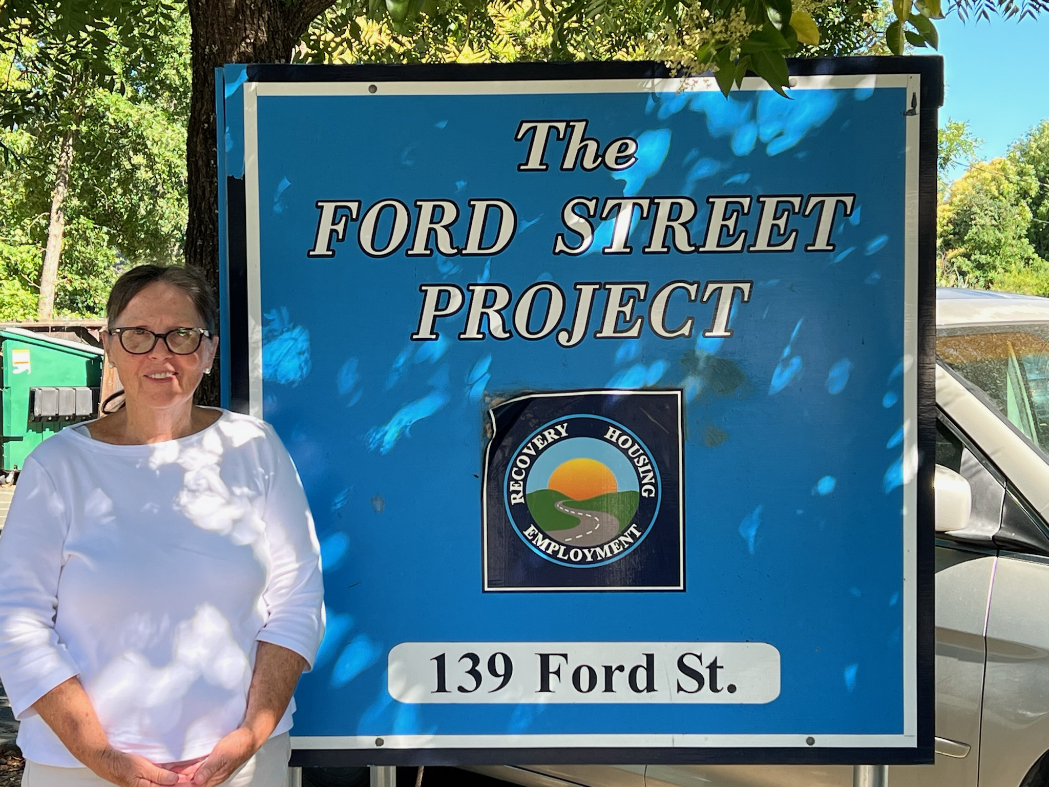 A photo of a woman standing by a sign that reads, "Ford Street Project."