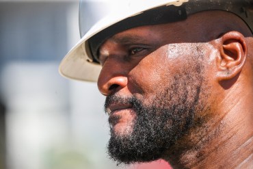 A photo of a man's face partially shaded by a hard hat in bright sunlight.