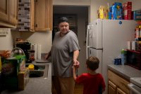 A photo of a father handing a popsicle to his young son inside an apartment.