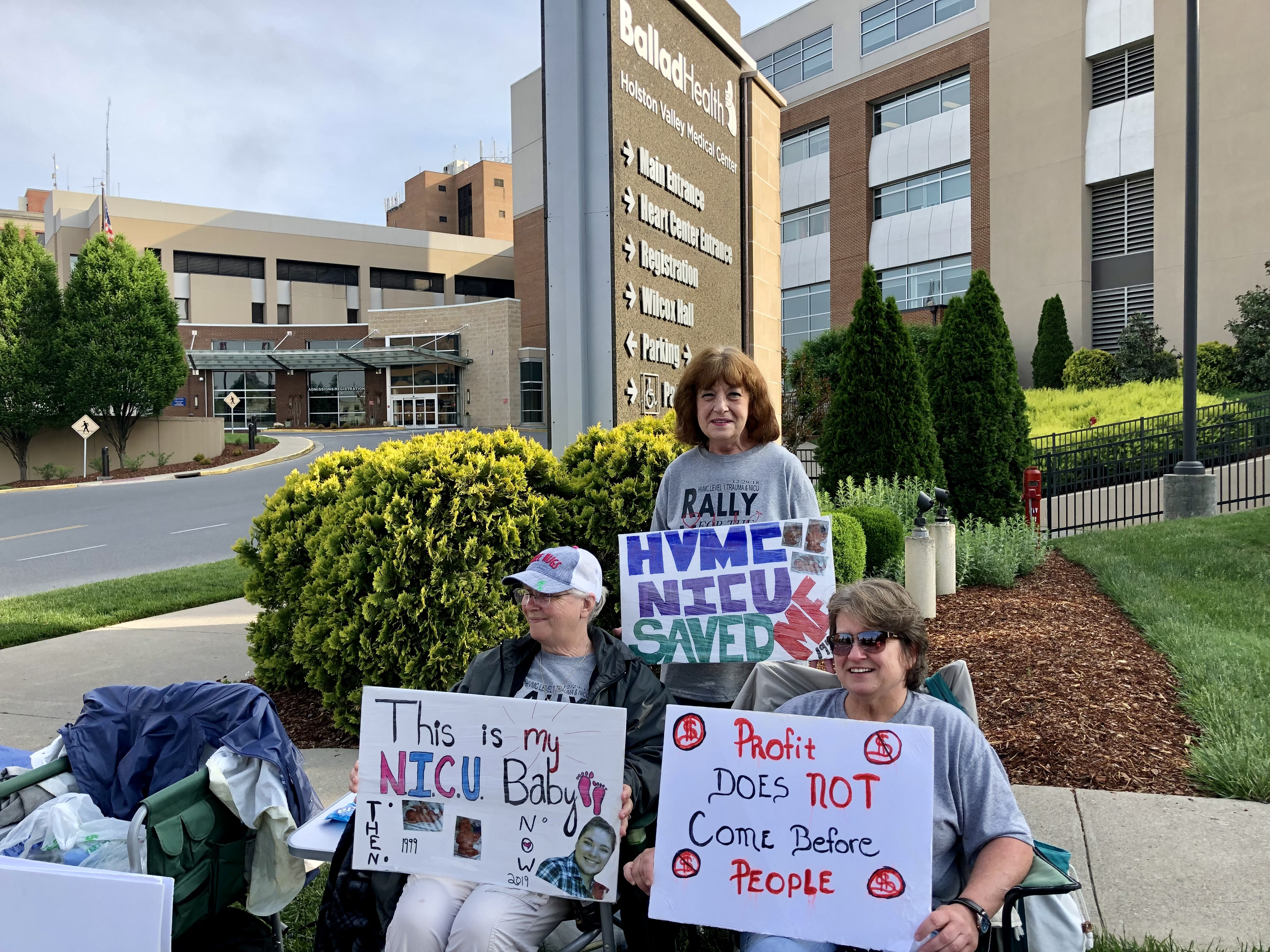 A photo of protesters with signs gathering outside of a hospital.