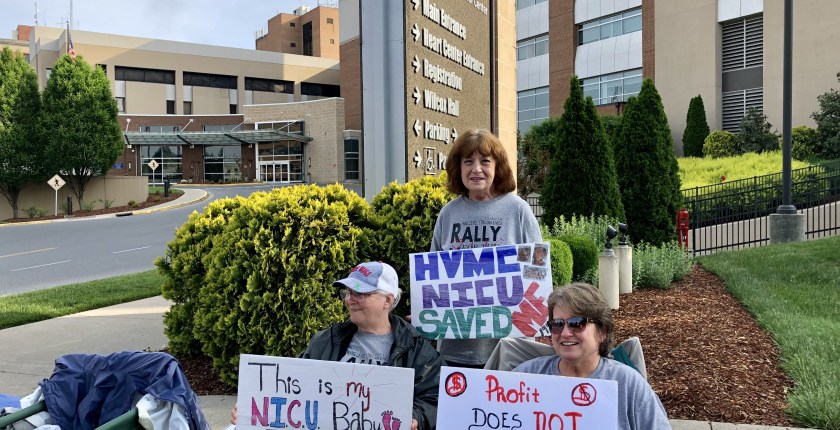 A photo of protesters with signs gathering outside of a hospital.